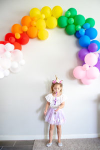 birthday girl under balloon rainbow