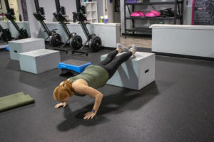 Heather doing a push up with her feet on a box at Kaia Fit